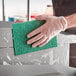 A person in gloves cleaning a metal surface with a green Lavex scouring pad.