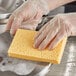 A person wearing a plastic glove cleaning a dishwashing sponge.