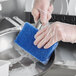 A person in a glove scrubbing a metal pan with a blue Lavex sponge.