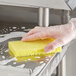 A hand in a glove using a yellow Lavex sponge to clean a stainless steel sink.