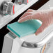 A hand in a clear glove using a green and white Lavex sponge to clean a stove top.