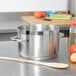 A Vollrath stainless steel sauce pot on a stove with a wooden spoon inside.