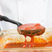 A person using a Vollrath High Heat Perforated Spoodle to scoop red sauce.