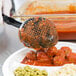 A black Vollrath High Heat Perforated Oval Nylon Spoodle over a plate of meatballs and vegetables.