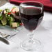A Libbey Gibraltar goblet of red wine next to a salad on a table with a white tablecloth.