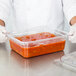 A person in gloves holding a Carlisle clear polycarbonate food pan filled with red sauce.