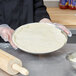 A person placing pizza dough in an American Metalcraft Super Perforated Pizza Pan.