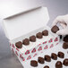 A gloved hand holding a heart-shaped chocolate candy in a box.