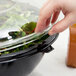 A hand using a Fineline clear plastic dome lid to cover a bowl of salad.