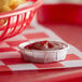 A small red Genpak container of ketchup with a basket of fries on a red and white checkered table.