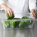A chef putting green peppers in a Rubbermaid clear polycarbonate food storage container.