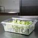 A Rubbermaid clear polycarbonate food storage box on a table with lettuce inside.