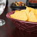 A raspberry oval weave basket filled with chips on a table.