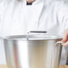 A woman in a white chef's coat holding a large silver Vollrath pot with a lid.