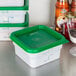 A stack of Cambro white square plastic containers with green lids.