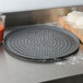 An American Metalcraft hard coat anodized aluminum pizza pan with perforations on a counter with dough.
