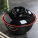 A black melamine bowl with a red rim containing chopsticks.