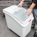 A person wearing gloves opens a white plastic container with a Rubbermaid sliding lid.