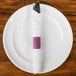A burgundy and white customizable paper napkin band wrapped around a fork and knife on a white plate.
