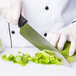 A gloved hand uses a Mercer Culinary Millennia chef knife to cut lettuce.