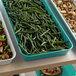 A green Cambro market pan filled with green beans and potatoes on a table.