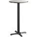 A round Lancaster Table & Seating bar height table with birch and ash reversible top on a cast iron base with a black pole.