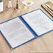A blue Choice 4-view menu cover on a table with silverware.