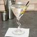A Libbey martini glass with liquid and olives in it.