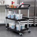 A black Rubbermaid utility cart with three shelves holding food items.