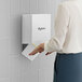 A woman using a white Dyson Airblade V hand dryer on a wall.