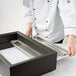 A person in a white chef's coat holding a Vollrath stainless steel steam table pan false bottom.