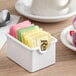 A white plastic sugar caddy with colorful sugar packets in it.