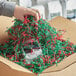 A hand using Spring-Fill red and green paper shred to pack a box.