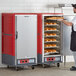 A man in a black apron using a Metro C5 red heated holding cabinet to display trays of bread.