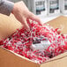 A hand putting Spring-Fill red and white shredded paper into a cardboard box.