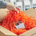 A hand holding a package of Spring-Fill orange shredded paper opening a box.