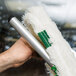 A hand using an Unger SwivelStrip T-Bar handle to clean a window with a white and green mop.