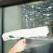 A hand using a Unger SwivelStrip T-Bar to clean a window.