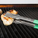 Two Vollrath Jacob's Pride tongs with green Kool Touch handles holding chicken on a grill.