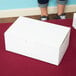 A person standing next to a white 8" x 5" x 3" cake box.