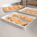 A Vollrath bun pan filled with cookies on a stainless steel counter.