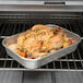 A Vollrath Wear-Ever baking and roasting pan with a roast chicken in it in an oven.