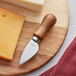 An Acopa stainless steel cheese spade on a cutting board with cheese.