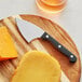 An Acopa stainless steel cheese cleaver on a cutting board with a slice of cheese.