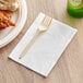 A plastic fork on a OneUp by Choice white dispenser napkin next to a plate of food.