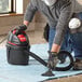 A man wearing a mask and gloves using a black and red Shop-Vac wet/dry vacuum to clean a carpet.