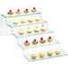 A Cal-Mil Glacier glass stair-step riser with small cupcakes on it.