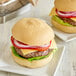 Two hamburgers on Schar Gluten-Free Sliced Hamburger Buns with lettuce and tomato on white plates.