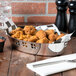 A Vollrath stainless steel oval bowl filled with fried chicken on a table.