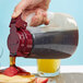A person pouring syrup from a Tablecraft dispenser onto pancakes.